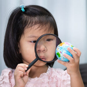 Young child looking at small globe through magnifying glass.