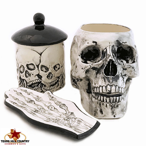 White ceramic skull cup, sugar bowl with skulls painted on them and skeleton hand spoon rest.
