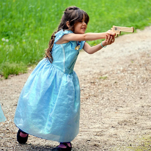 Girl dressed as princess with wooden toy revolver.