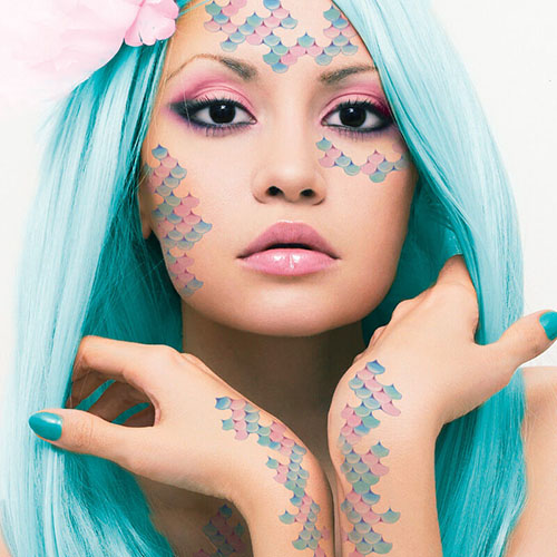 Temporary tattoos of pink and light blue mermaid scales on face and arms.