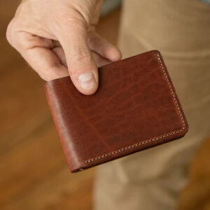 Hand holding brown leather bi-fold wallet.