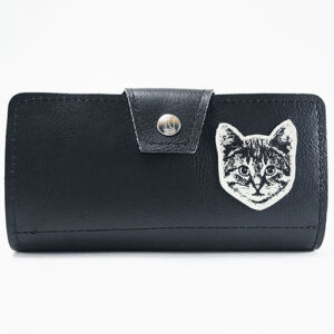 Black vinyl clutch wallet with cat face cutout on it by Couch.