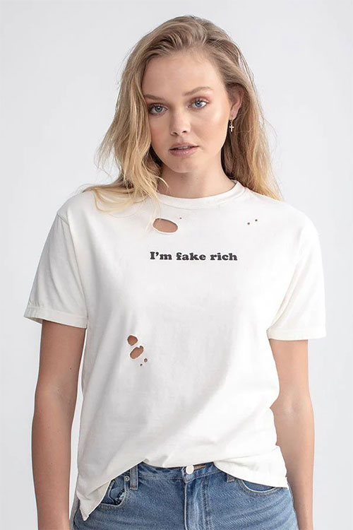 Young woman wearing white t-shirt with small holes in it and 'I'm fake rich' written across the chest.