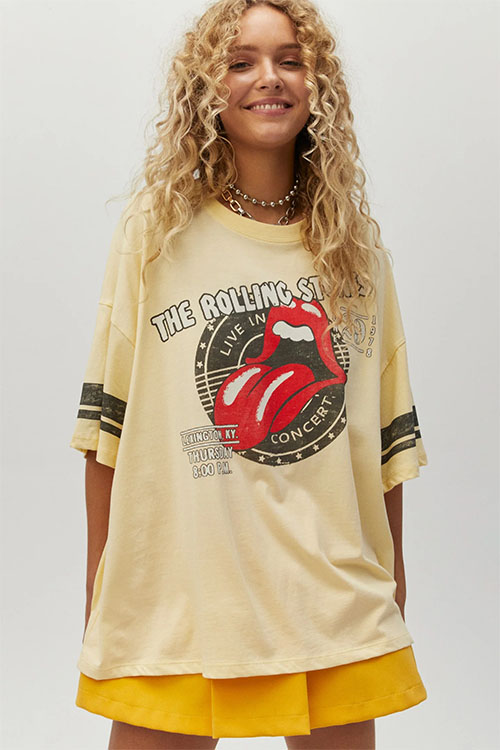 Girl wearing oversized light-yellow t-shirt with Rolling Stones band logo.