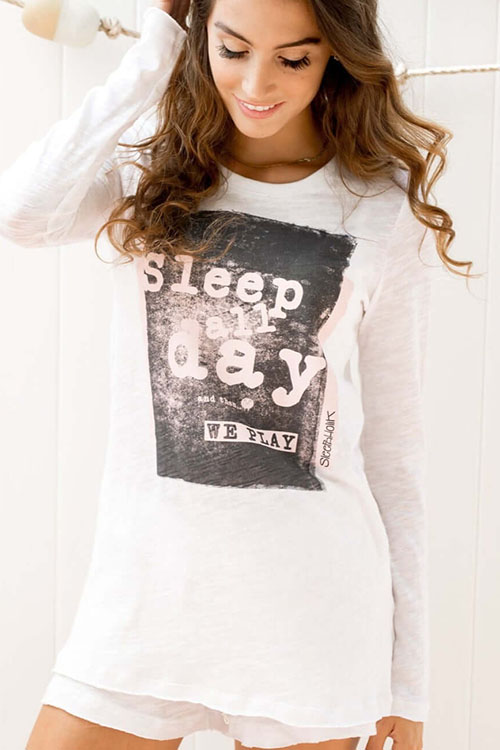 Woman wearing white, long sleeve t-shirt with night-scape print on the front with words 'sleep day'.