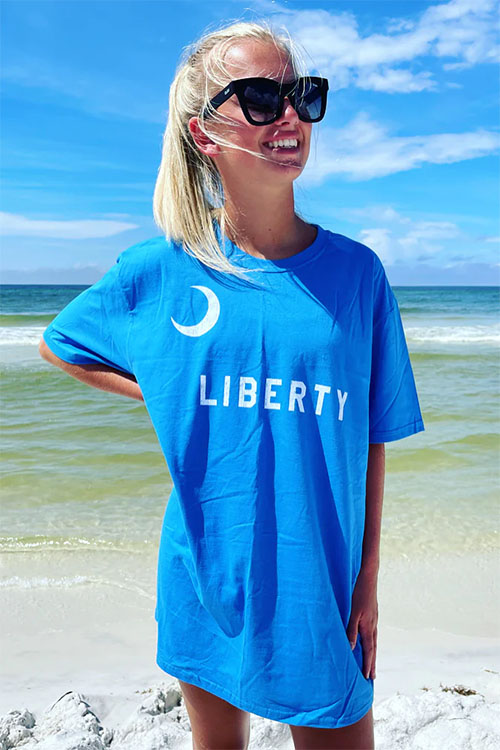 Young woman wearing blue t-shirt with white crescent moon and the word 'liberty' on the chest.