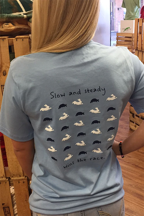 Woman wearing grey t-shirt with hares and tortoises on the back, with words 'slow and steady wins the race'.