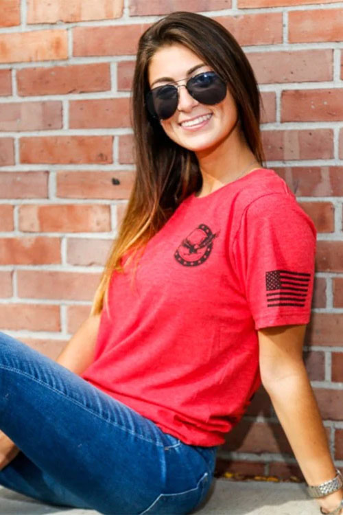 Woman wearing red t-shirt with small Love of country logo on chest and American flag on arm.