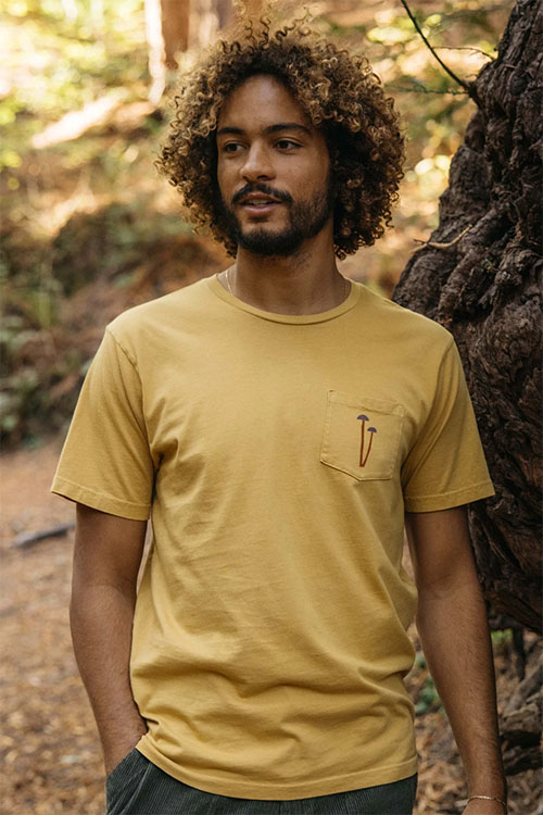 Man wearing light yellow t-shirt with front pocket with mushroom design print.