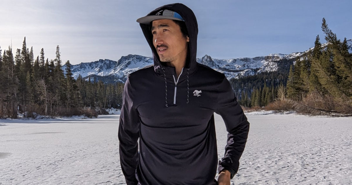 Man standing in snowy landscape wearing black athletic hoodie and cap.