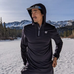 Man standing in snowy landscape wearing black athletic hoodie and cap.